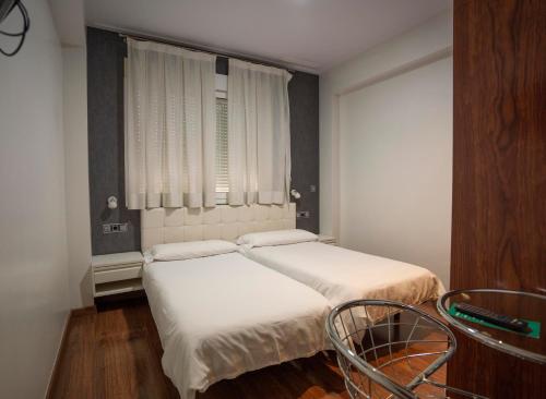 a bedroom with two beds and a chair and a window at Hotel Lluna in Alzira