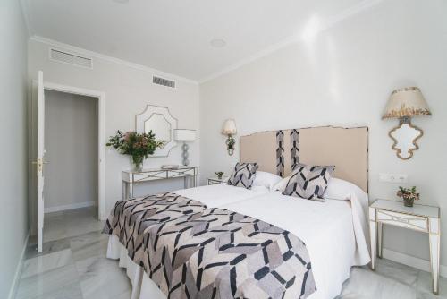 ein weißes Schlafzimmer mit einem Bett mit einer schwarzen und weißen Bettdecke in der Unterkunft Apartamentos Abreu Suites in Sevilla