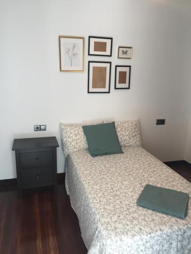 1 dormitorio con 1 cama, mesita de noche y cuadros en la pared en Atico Vilagarcia, en Vilagarcía de Arousa