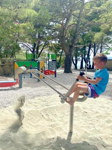 a young boy sitting on a swing in a playground at Family Resort Urania in Baška Voda