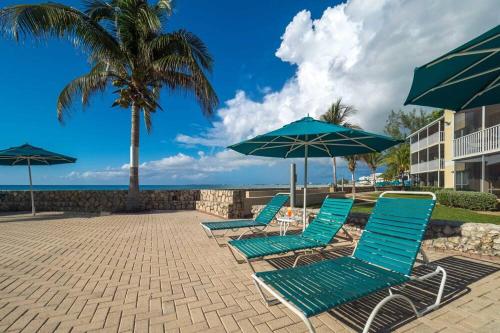 a group of blue lounge chairs and umbrellas at Beach Living at Plantation Village BLGS in George Town