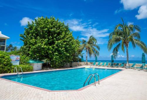 a swimming pool with palm trees and the ocean at Beach Living at Plantation Village BLGS in George Town