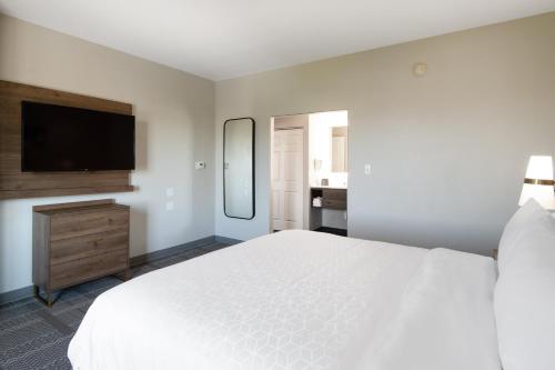 a white bedroom with a large bed and a flat screen tv at Staybridge Suites Phoenix Glendale Sports Dist by IHG in Glendale