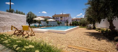 a swimming pool in a yard with chairs and umbrellas at A Casa da Cerca in Almodôvar