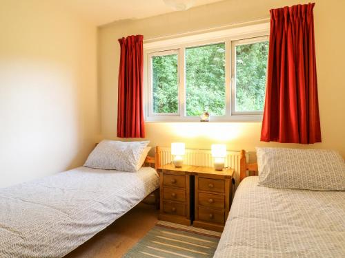 two twin beds in a room with red curtains at Barks Cottage in Whiston