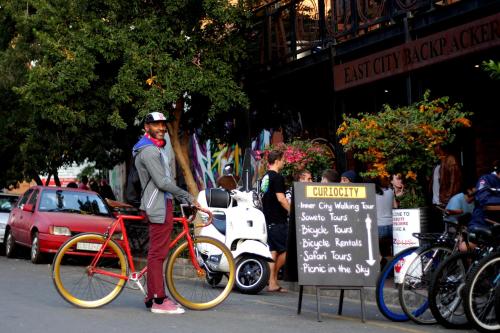 un hombre está parado en una bicicleta en la calle en CURIOCITY Backpackers Johannesburg, en Johannesburgo