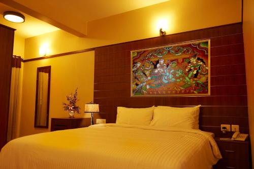 a bedroom with a large bed with a painting on the wall at Srivar Hotels in Guruvāyūr