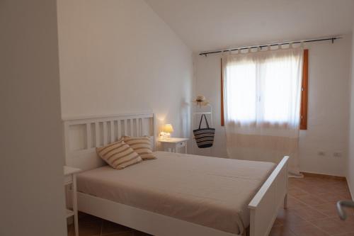 a white bedroom with a bed and a window at DomoMea - Villetta Chia in Domus de Maria