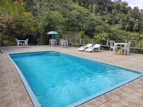 ein blauer Pool mit Stühlen und einem Sonnenschirm in der Unterkunft Chalés & Casas Shallon Adonai in Visconde De Maua