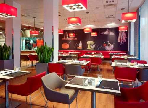 ワルシャワにあるibis Warszawa West Stationのテーブル、椅子、赤い椅子が備わるレストラン