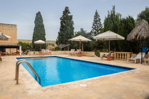 a swimming pool with chairs and umbrellas in a yard at Ta' Bertu Host Family Bed & Breakfast in Ħal Far
