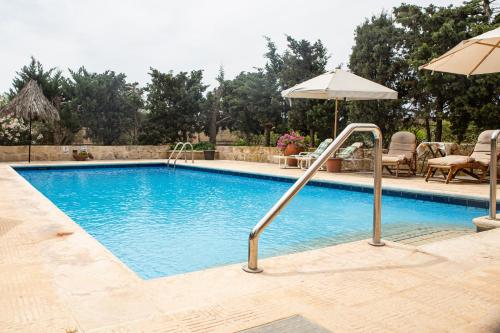 a swimming pool with an umbrella and chairs and a table at Ta' Bertu Host Family Bed & Breakfast in Ħal Far