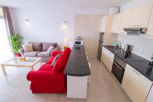 a living room with a red couch and a kitchen at MEDANO4YOU The Harbour Holiday Home in El Médano