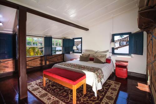 um quarto com uma cama com um banco vermelho e janelas em Pousada Bartholomeu em Paraty