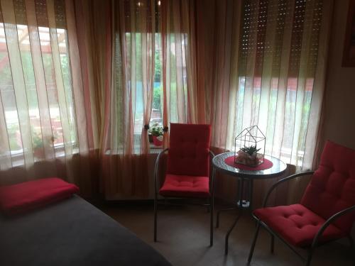 - une chambre avec 2 chaises rouges, une table et des fenêtres dans l'établissement Betty Apartman, à Balatonfůzfő