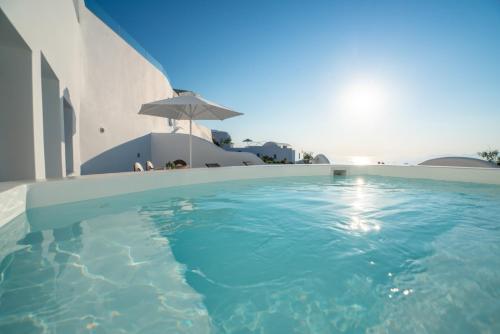 a swimming pool in front of a building with an umbrella at Sun Angelos Oia - Luxury Cave Suites in Oia