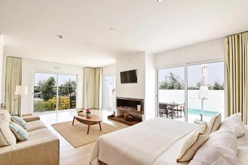 a white bedroom with a large bed and a living room at Sesmarias Turismo Rural & SPA in Peroguarda