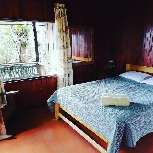 a bedroom with a bed with a blue blanket and a window at Pochotel Natural in Turrialba