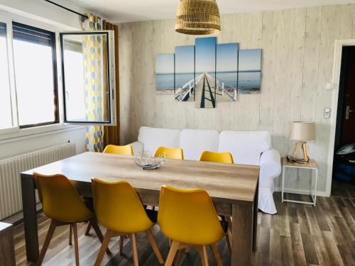 a dining room with a wooden table and yellow chairs at Le Foch in Ouistreham