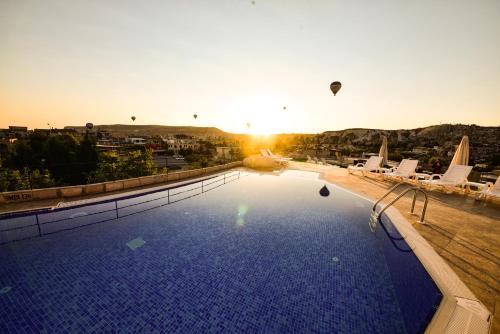 a swimming pool with the sun setting in the background at Cappadocia Caves Hotel in Goreme