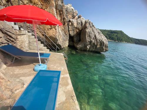 a red umbrella and chairs and a swimming pool in the water at Apart Lux Beciragic in Dobra Voda