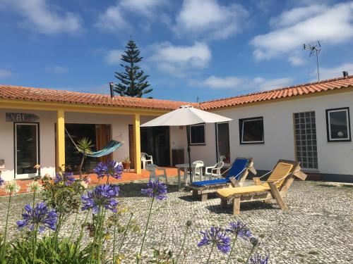 a house with chairs and an umbrella and purple flowers at Vagos Art.Lab in Vagos