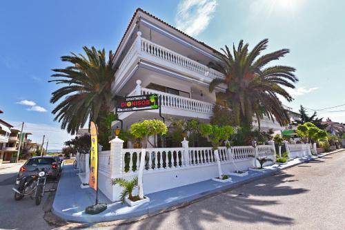 biały budynek z palmami na ulicy w obiekcie Dionisos Palms Apartments w mieście Paralia Dionisiou