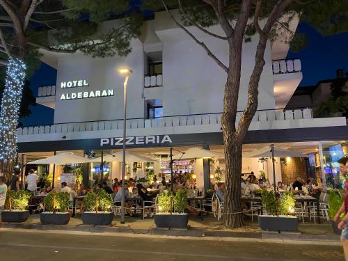 personas sentadas en mesas fuera de un restaurante por la noche en Hotel Aldebaran, en Lido di Jesolo