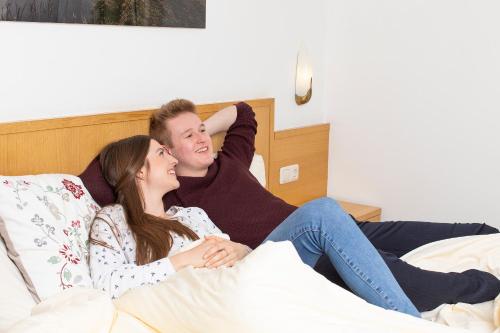 a man and a woman sitting on a bed at Hotel garni Weberhäusl in Strobl