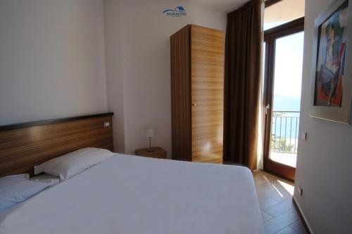 a bedroom with a white bed and a large window at Nuraghe Apartments in Teulada