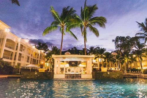 a resort swimming pool with palm trees and a building at Beach Club Palm Cove 2 Bedroom Luxury Penthouse in Palm Cove