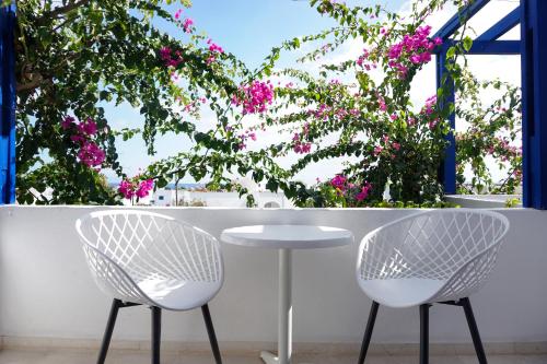 two chairs and a table in front of a window with pink flowers at Proteas Hotel in Kamari