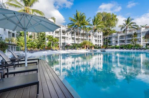 a swimming pool with an umbrella and chairs and buildings at Beach Club Palm Cove 2 Bedroom Luxury Penthouse in Palm Cove