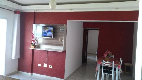 a living room with a red wall with a dining room at Edifício Santorini in Mongaguá