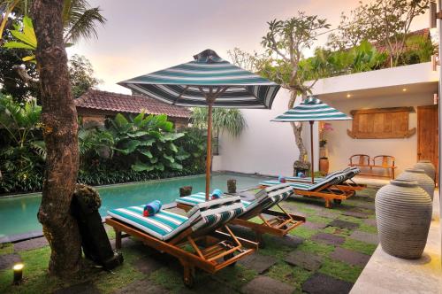 a group of chairs and umbrellas next to a pool at Room & Vespa 1 in Seminyak
