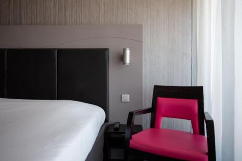 a pink chair sitting next to a bed in a room at Hôtel Le Nautic in Arcachon