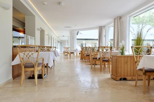 un restaurante con mesas y sillas blancas y ventanas en Hotel Residenz WALDOASE en Ahlbeck