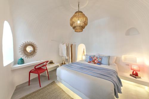 1 dormitorio blanco con 1 cama y 1 silla roja en White Cave by Caldera Houses, en Oia