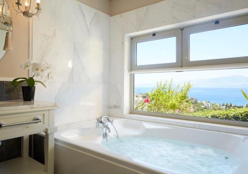 een witte badkamer met een bad en een raam bij Pleiades Luxurious Villas in Agios Nikolaos