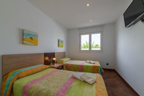 a bedroom with two beds and a tv and a window at Villa Santandria Grupo Seranova Luxury Hotel in Ciutadella