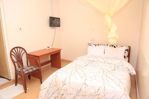 1 dormitorio con cama, silla y escritorio en The 4 JS Bed and Breakfast Emali, en Emali