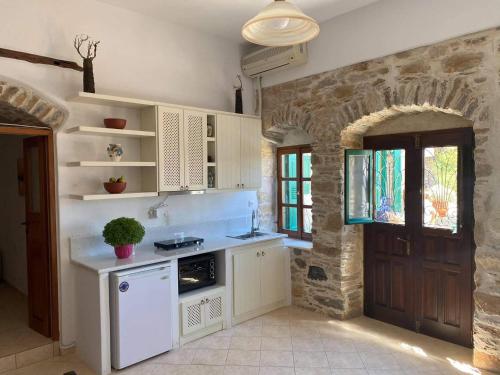 cocina con armarios blancos y pared de piedra en Pension Sofia Amorgos, en Katápola