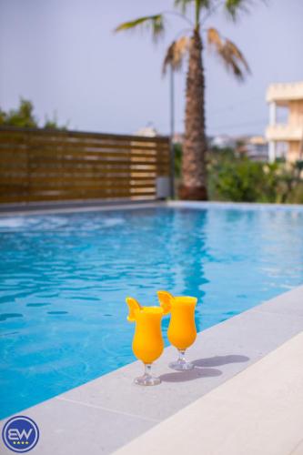 two yellow glasses sitting next to a swimming pool at Blue Water Hotel Ksamil in Ksamil