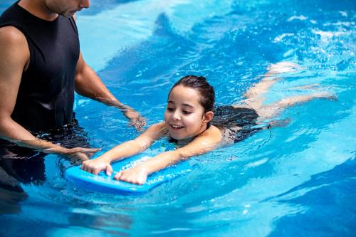 a young girl laying on aogie board in a swimming pool at Centara West Bay Hotel & Residences Doha in Doha