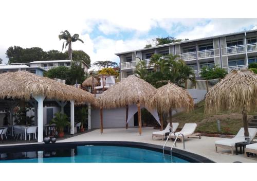 a resort with a swimming pool with chairs and straw umbrellas at Studio Caliente vue panoramique Rocher du Diamant in Le Diamant
