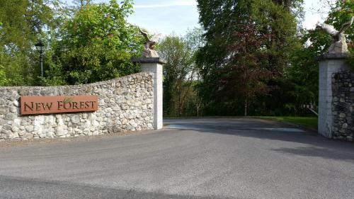 a stone wall with a new forest sign next to a road at New Forest Estate Lodges in Tyrrellspass