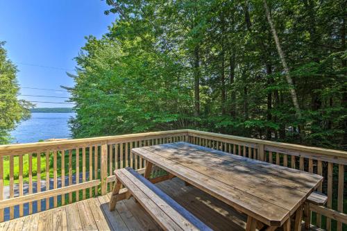 a wooden deck with a wooden picnic table on the side of a lake at Sebago Lake Gem on Private Cove with Boat Dock! in Raymond