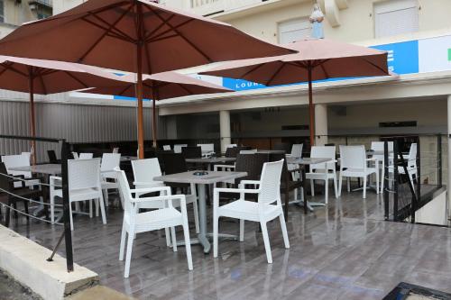 un restaurant avec des chaises blanches, des tables et des parasols dans l'établissement Hôtel Marquette, à Lourdes