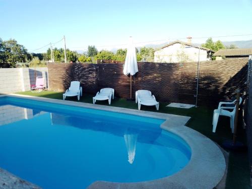 a swimming pool with three chairs and a umbrella at Apartamentos Rurales Tierras de Granadilla in Zarza de Granadilla