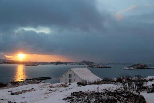 a house on the shore of a body of water with the sunset at Sveggvika Guesthouse in Averoy